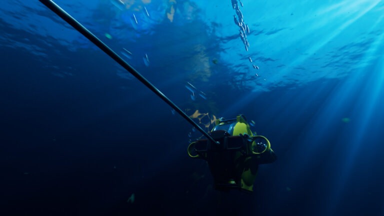Deep Trekker: ROV DTG3: Gul undervandsdrone med kabel set bagfra under den lyse vandoverflade, med skrå solstråler og en stime småfisk ovenover